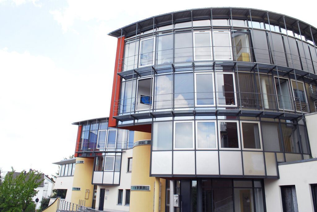 Ein modernes, mehrstöckiges Gebäude aus Glas und Stahl mit geschwungener Architektur, dargestellt in einem unscharfen Bild.