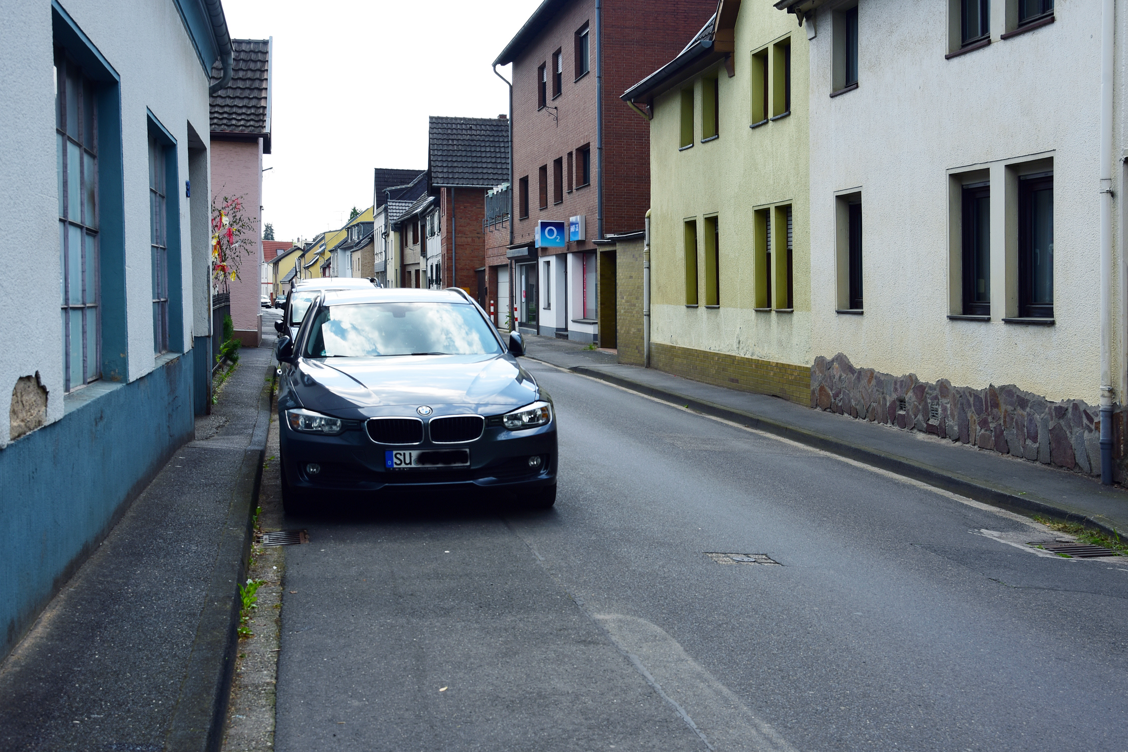 Ein schwarzes Auto parkt auf der Brunnenstraße in Bornheim-Roisdorf die von mehrstöckigen Häusern mit schmalen Gehwegen gesäumt ist.