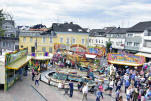 Septemberkirmes in Bornheim mit bunten Fahrgeschäften und Buden, umgeben von Besuchern, auf dem Peter-Fryns-Platz in Bornheim, mit Wohngebäuden im Hintergrund.