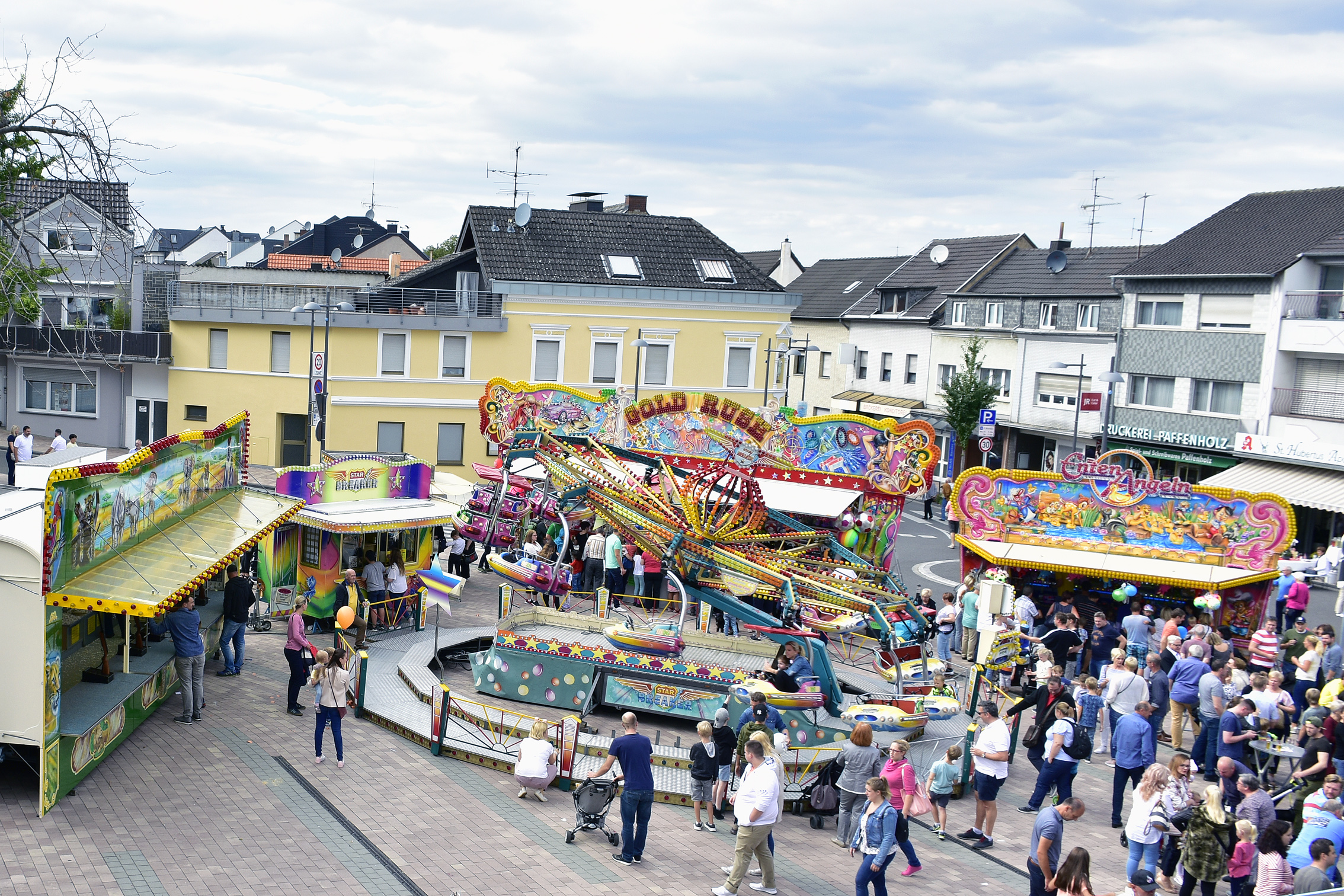 Septemberkirmes in Bornheim mit bunten Fahrgeschäften und Buden, umgeben von Besuchern, auf dem Peter-Fryns-Platz in Bornheim, mit Wohngebäuden im Hintergrund.
