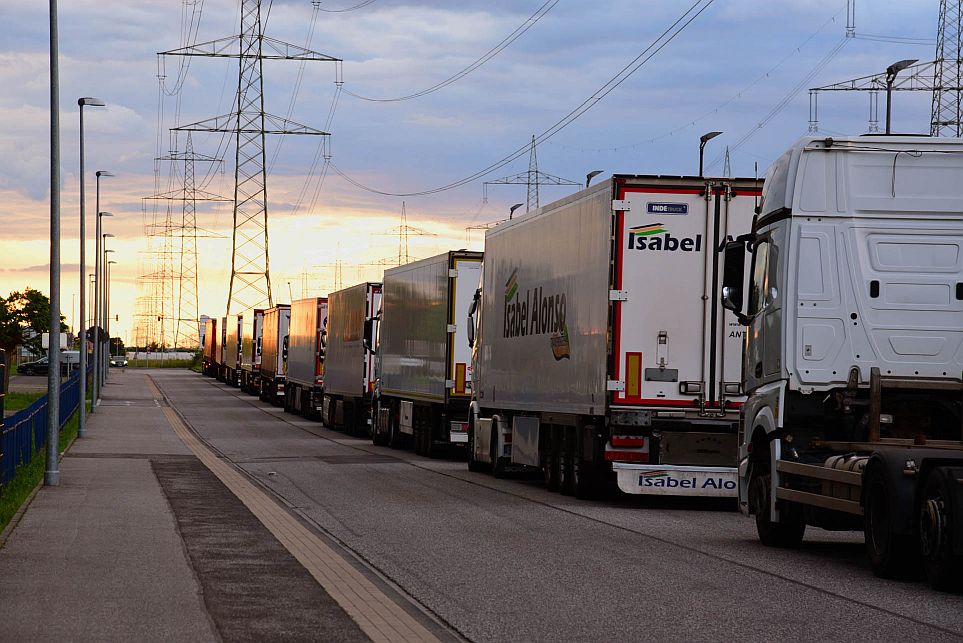 Eine Reihe geparkter Lastwagen ist bei Sonnenuntergang entlang einer Straße in der Nähe von Stromleitungen zu sehen.