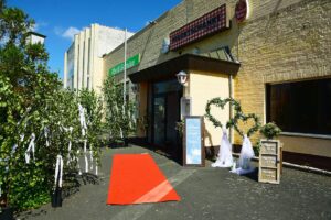 Der Eingang der Marktschänke mit rotem Teppich, herzförmiger Dekoration mit Grünzeug und einem Willkommensschild ist für ein besonderes Ereignis unter sonnigem Himmel hergerichtet.