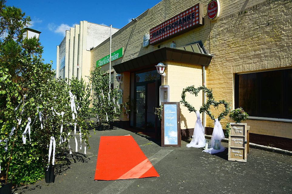 Der Eingang der Marktschänke mit rotem Teppich, herzförmiger Dekoration mit Grünzeug und einem Willkommensschild ist für ein besonderes Ereignis unter sonnigem Himmel hergerichtet.