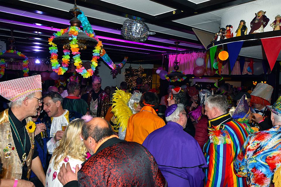 Eine Karnevalsparty mit Menschen in farbenfrohen, festlichen Kostümen und Dekorationen wie Luftschlangen, Wimpeln und hängenden Ornamenten.